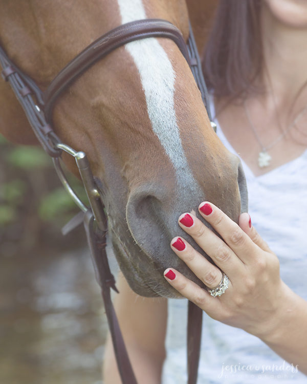 close up of woman's hand with red nail polish and diamond ring petting her horse's nose
