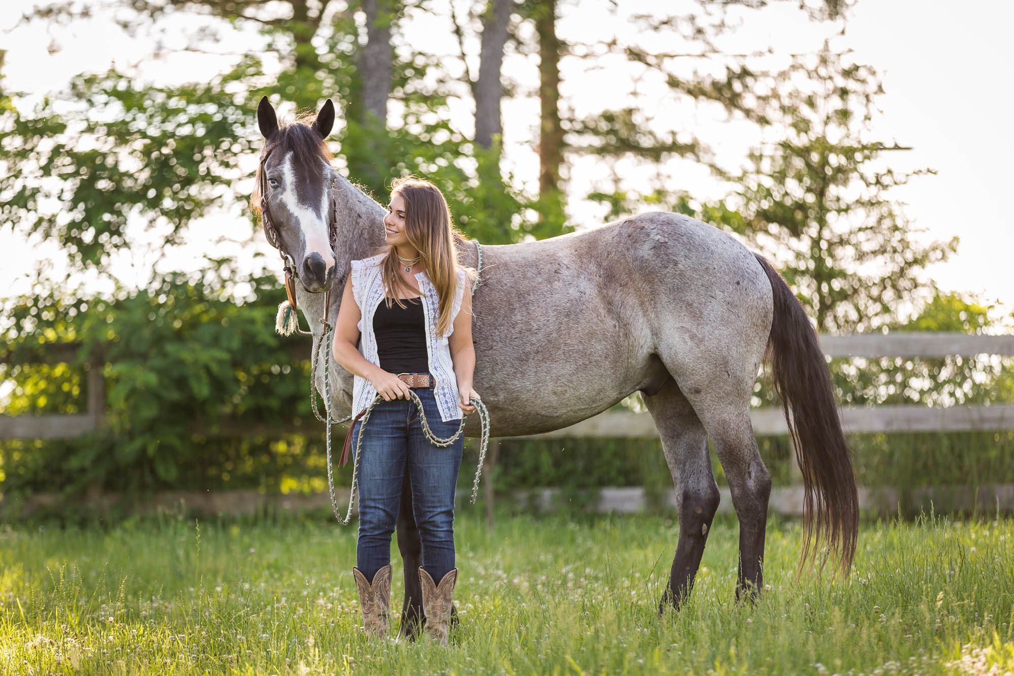 girl standing next to and looking at her gray mustang horse