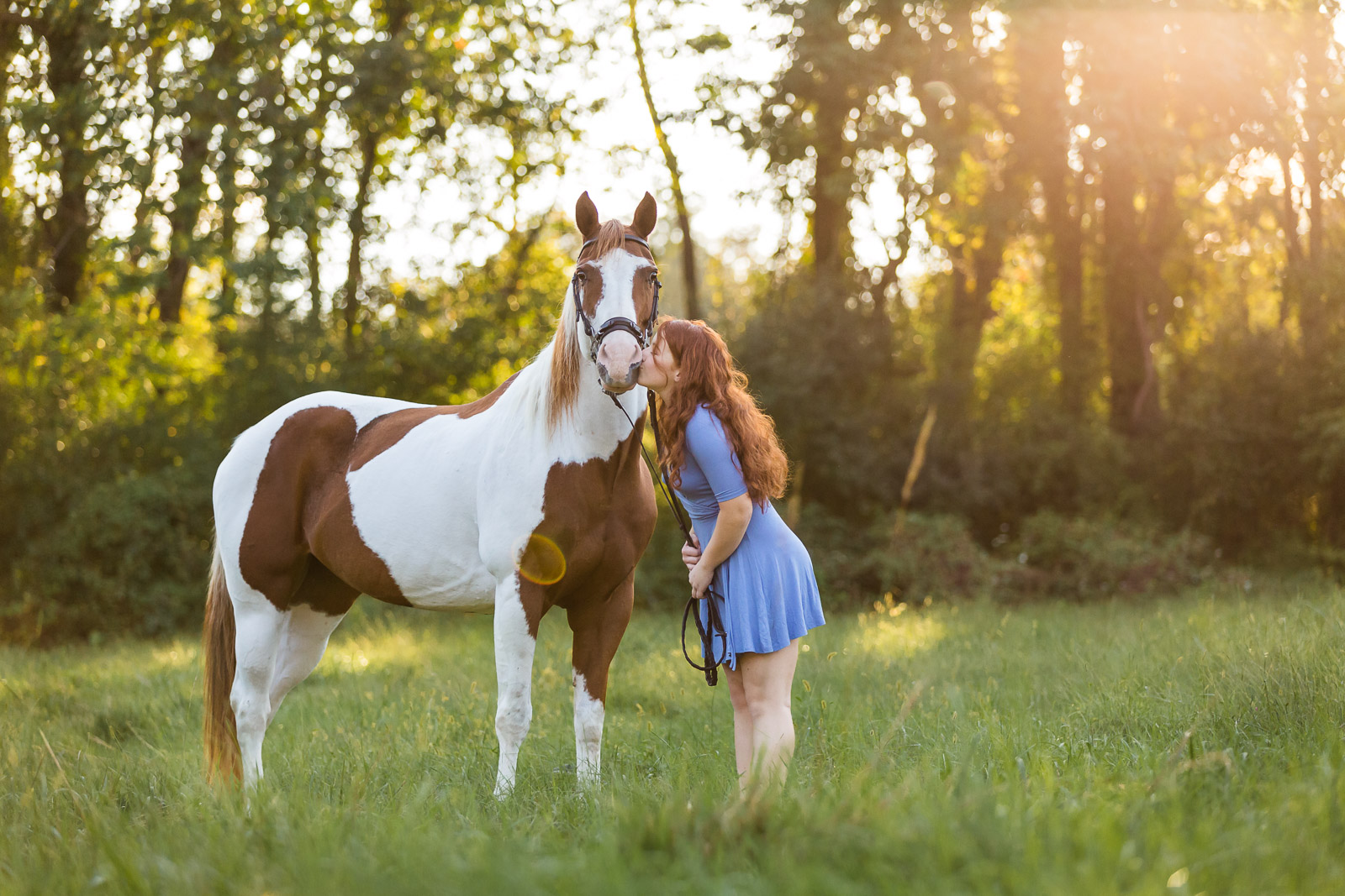 redheaded girl kissing horse in field