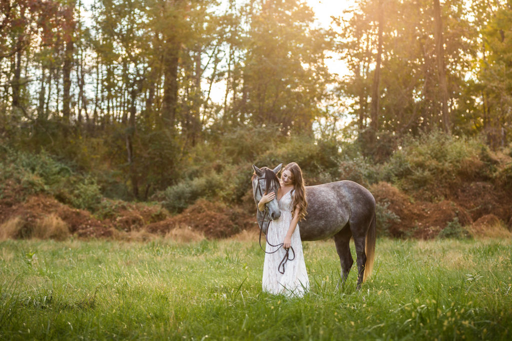 girl in white dress with dapple grey pony in field