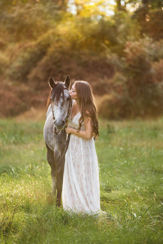 girl in white dress kissing dapple grey pony
