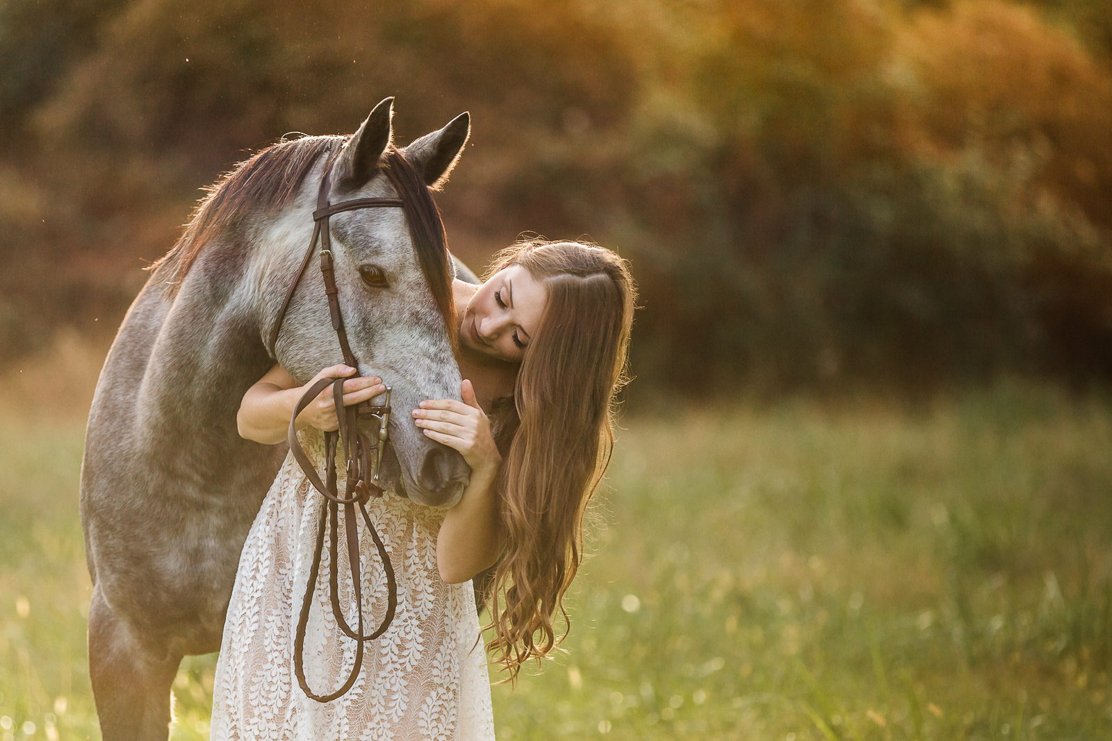 girl in white dress leaning down next to grey horse