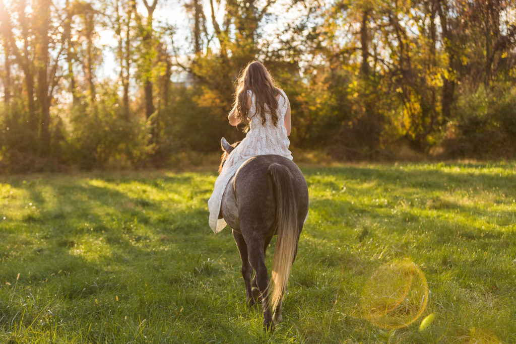 girl in white dress on grey pony at sunset