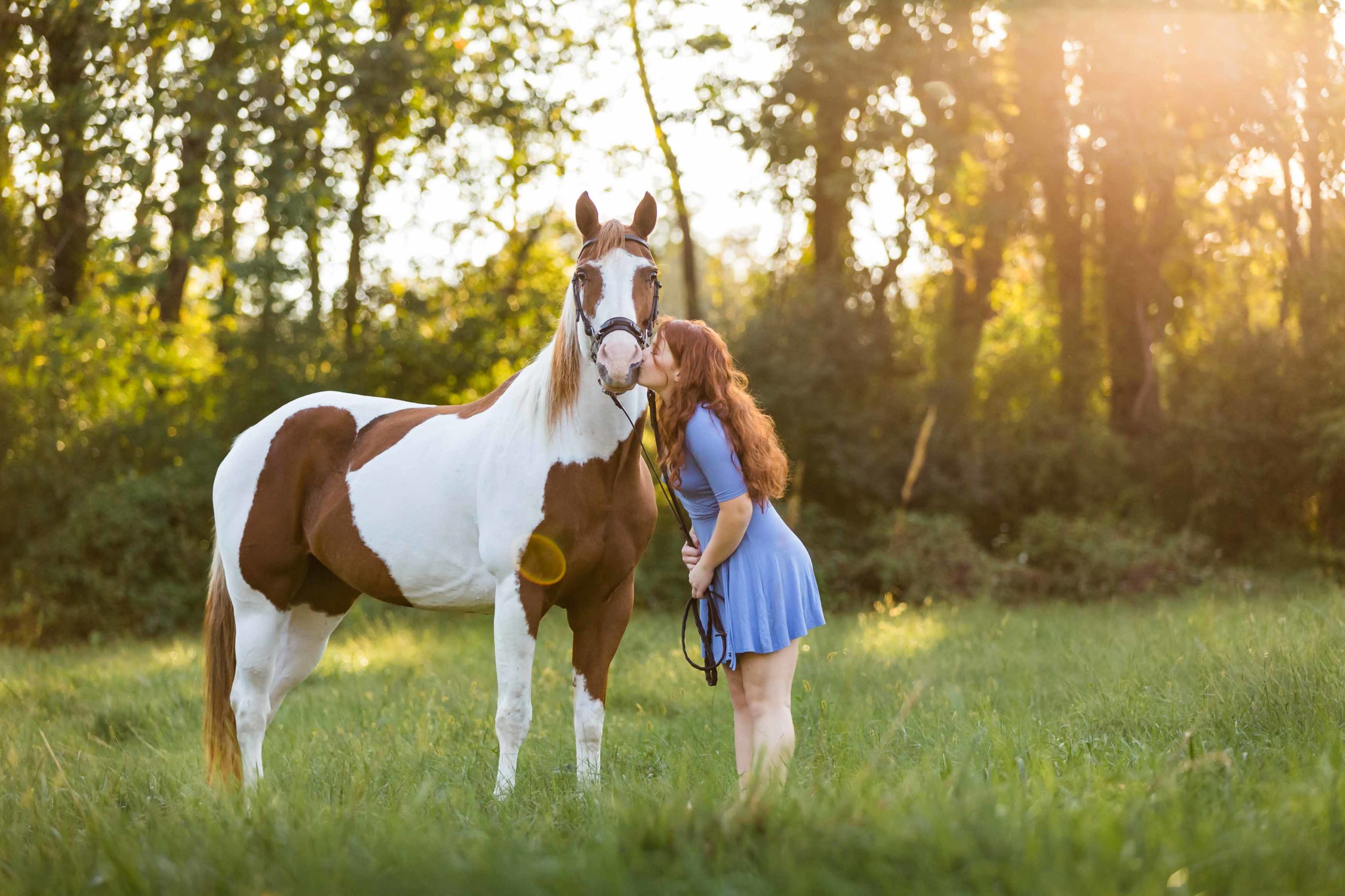 girl in blue dress kissing paint horse