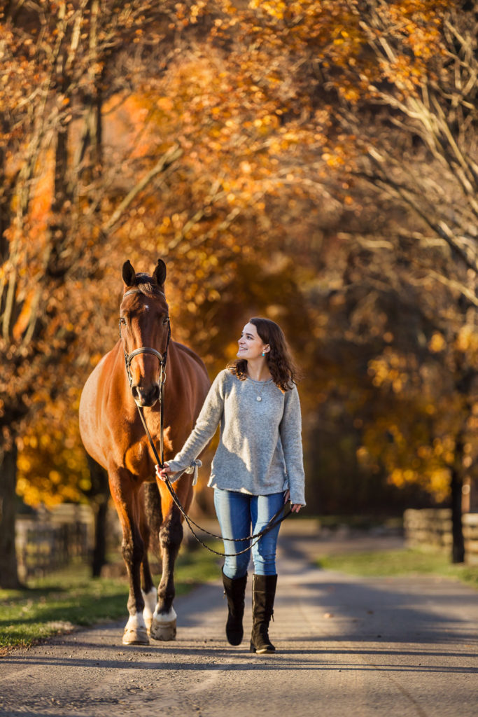 girl walking horse through fall leaves at Hunters Crossing Farm