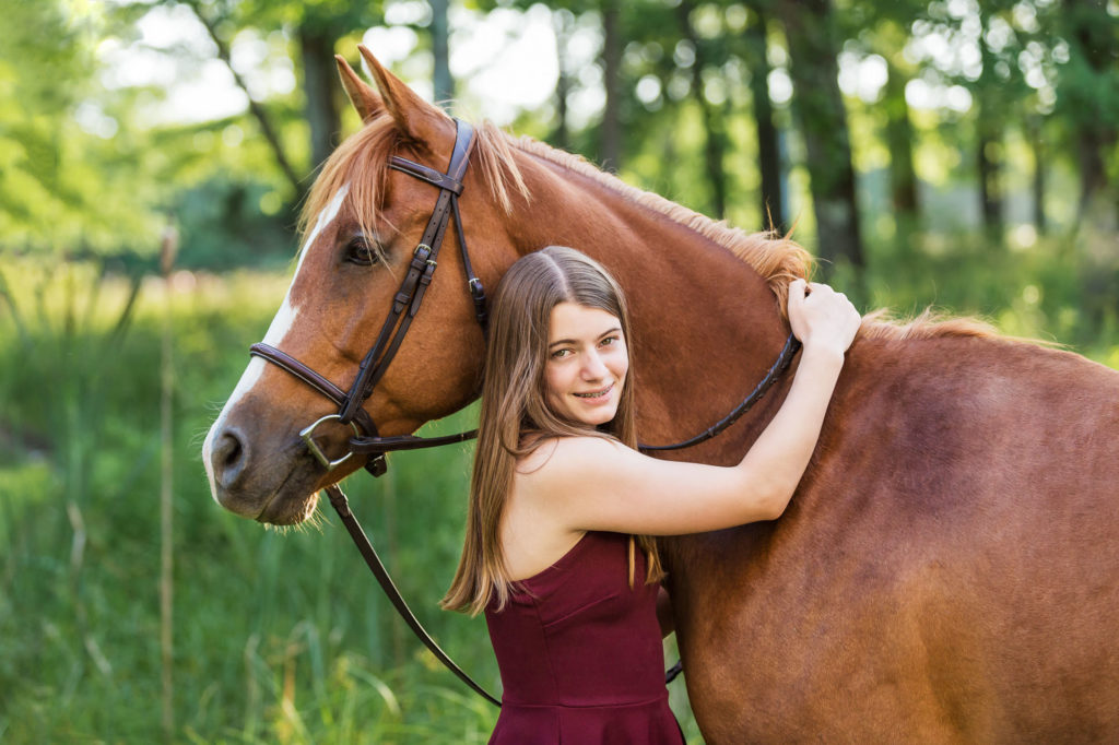 girl in burgundy dress hugging her chestnut mare