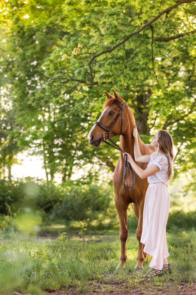 girl in pink skirt and white top with her horse in the trees