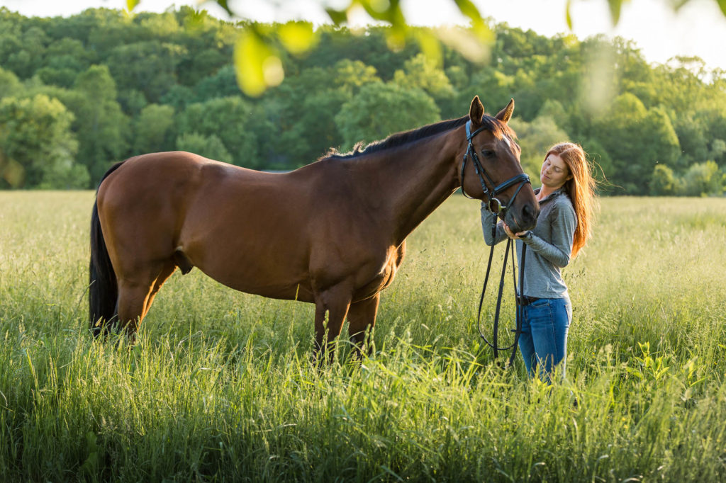 red headed girl in gray shirt with bay horse in field at Golden Gait Farm