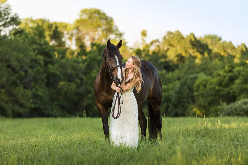 blond girl in white dress in field with bay horse