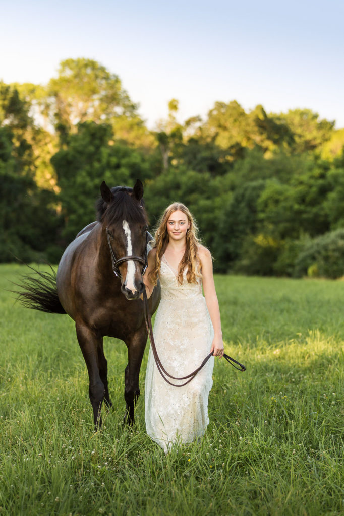 blond girl in white dress walking bay horse through field