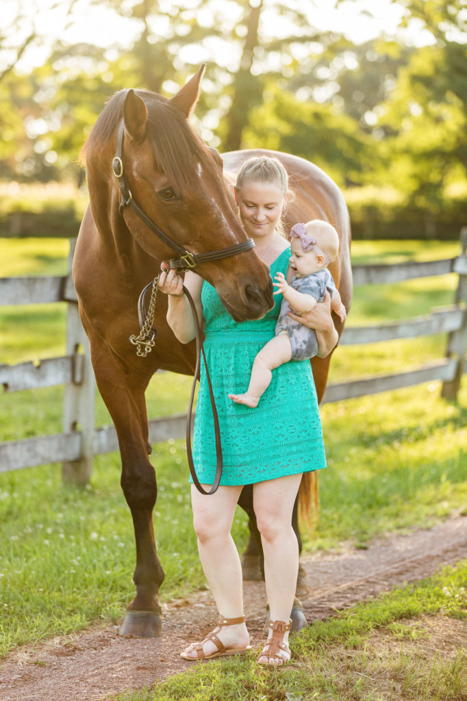 woman holds her baby up to her horse and baby touches horse's muzzle