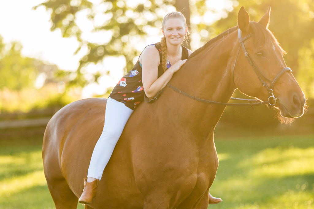 woman in white jeans with braided hair on her horse in the sun
