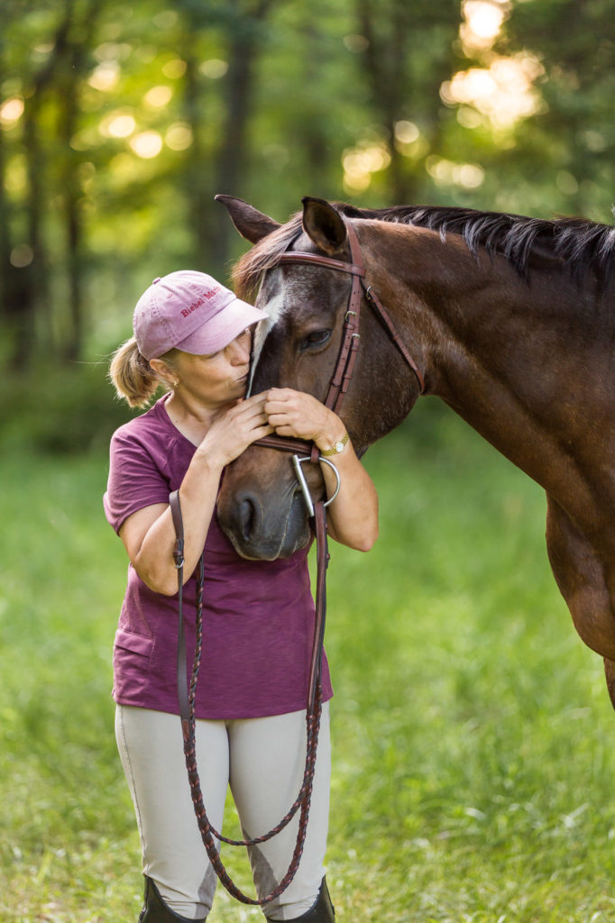 woman in mauve top hugging her horses's face