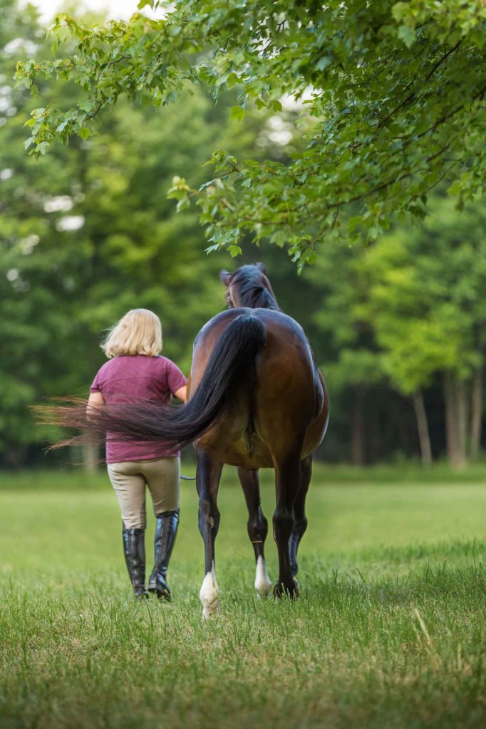 woman walking away with her horse across a field