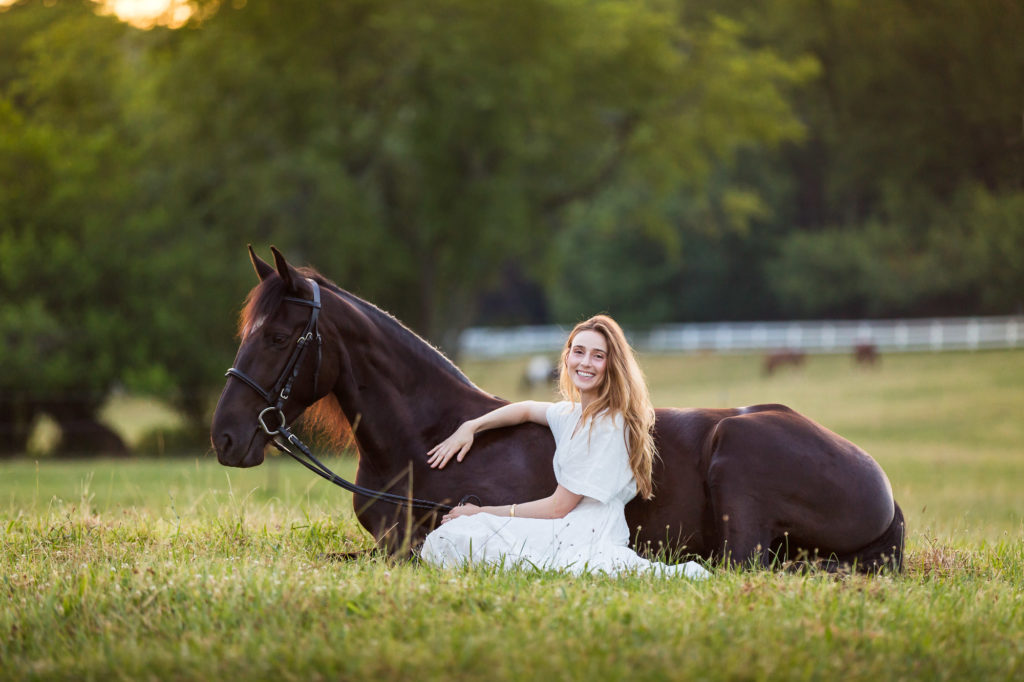woman sitting on ground next to black horse
