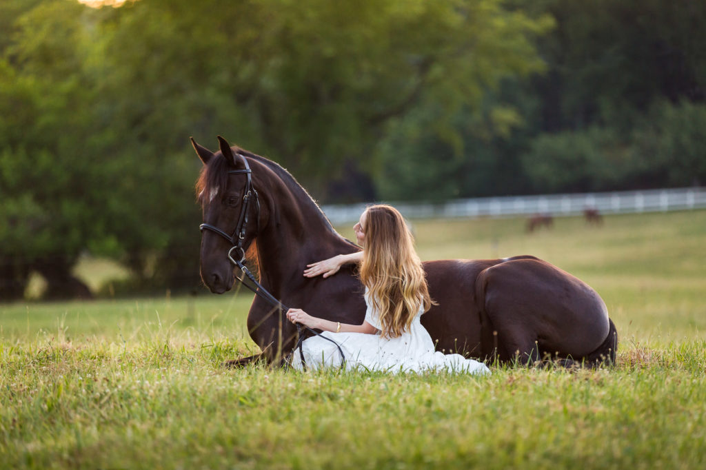 woman on ground with black horse in the grass