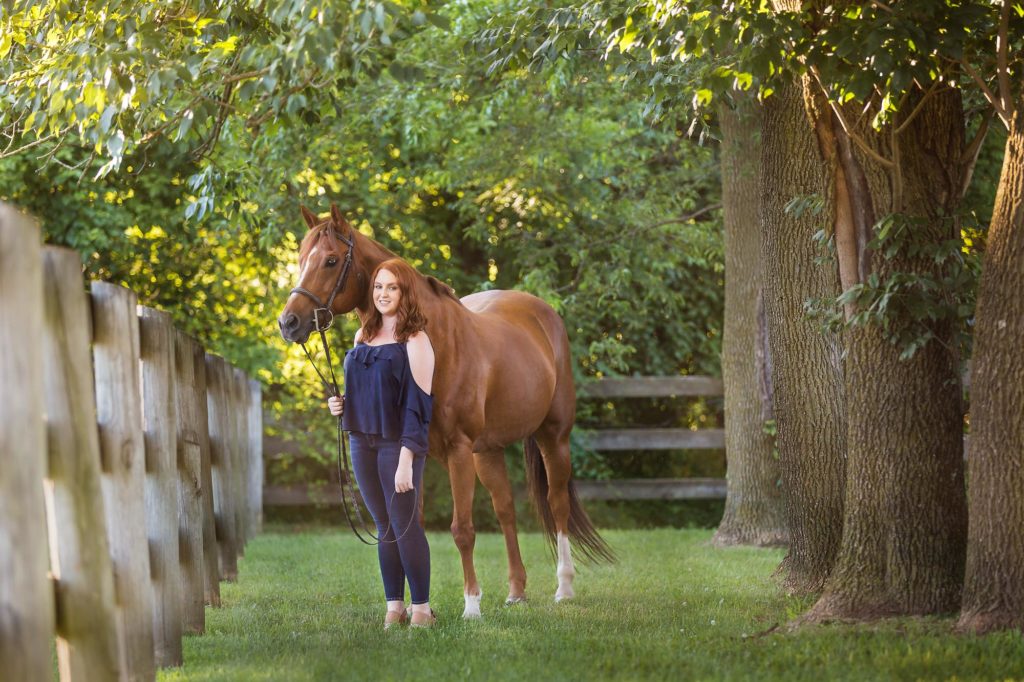 girl with red hair holding horse under the trees at Sommerfield Stables