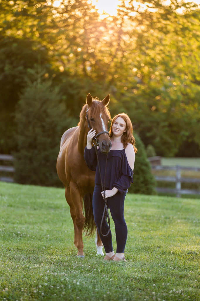 girl with red hair holding horse in grassy field
