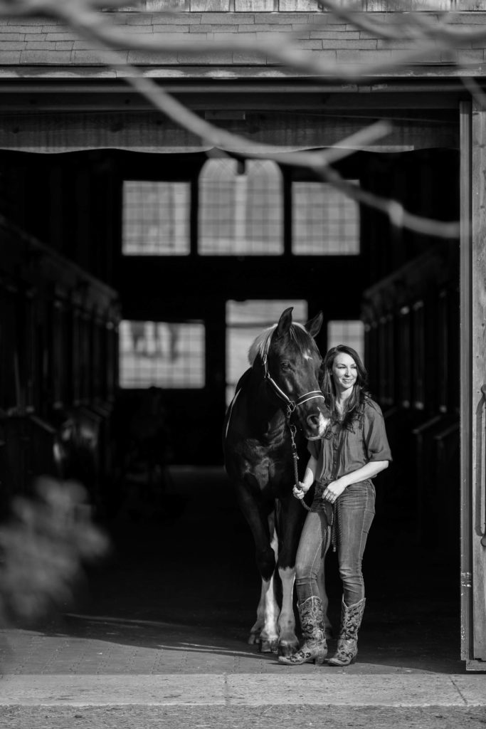 black and white image of girl in front of barn at Footlight Farm with horse