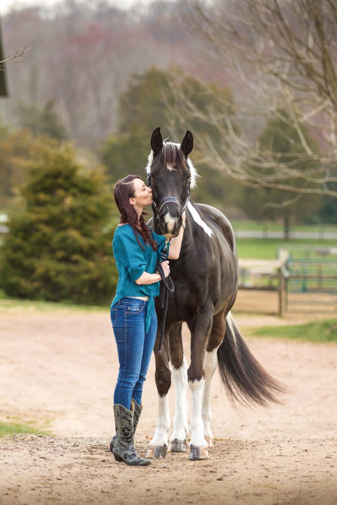 girl in teal top kissing black and white horse at Footlight Farm