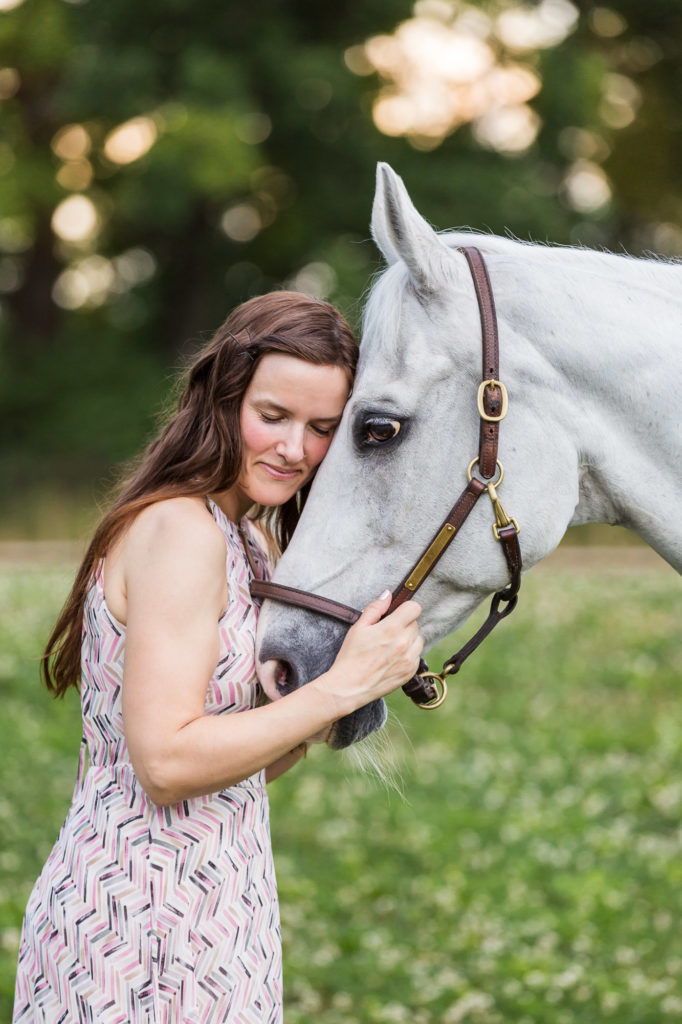 woman with long brown hair cuddling her white horse