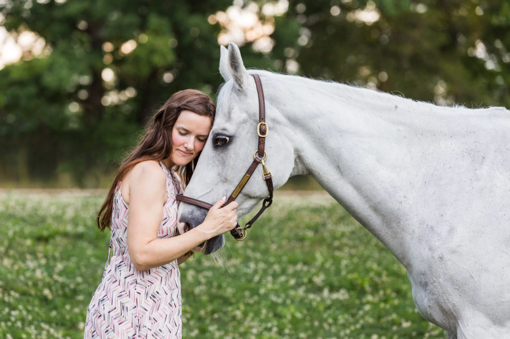 girl in pink dress with long brown hair cuddling her white horse's face at Duck Crossing Farm