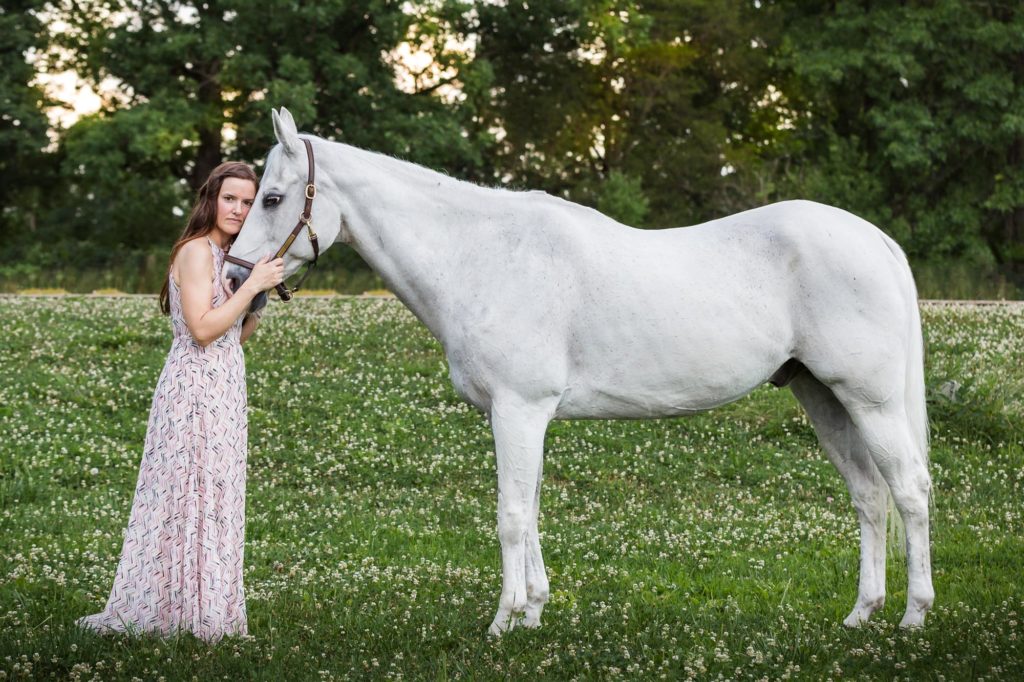 girl in pink dress holding the face of her white gelding at Duck Crossing Farm