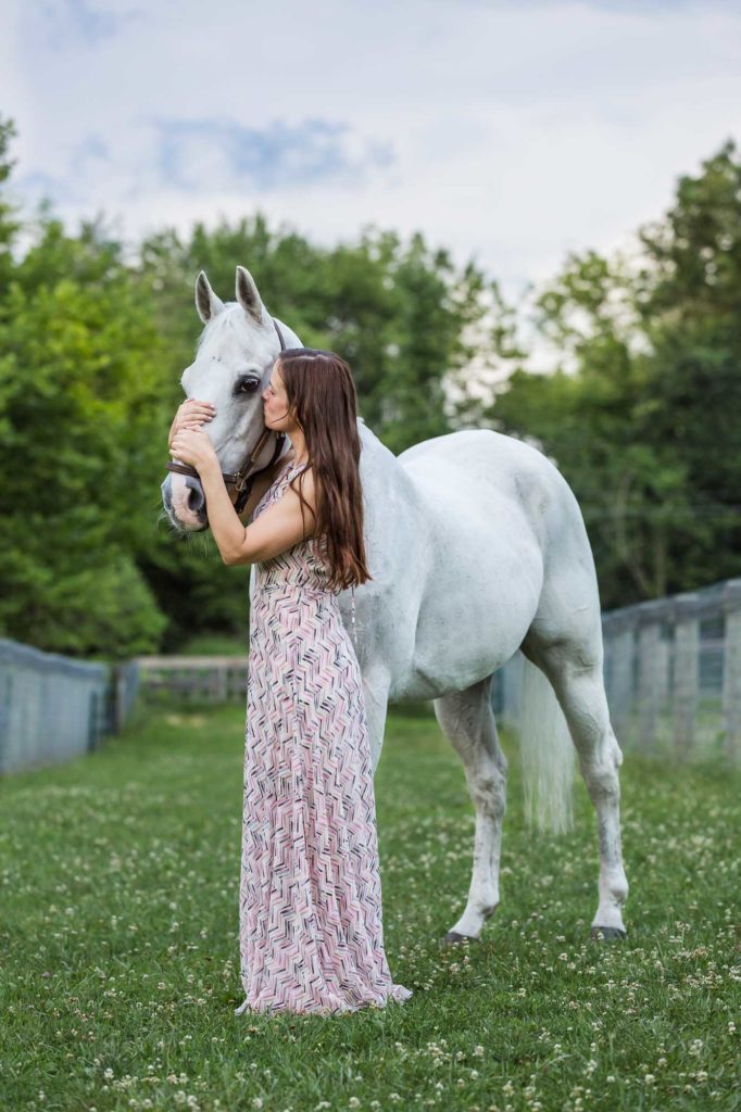 long haired girl in pink dress kissing her white horse at Duck Crossing Farm