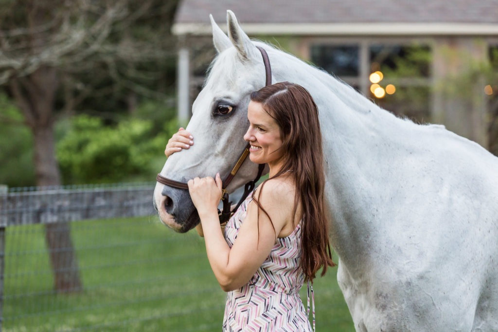 woman with long brown hair holding her white horse by the halter at Duck Crossing Farm