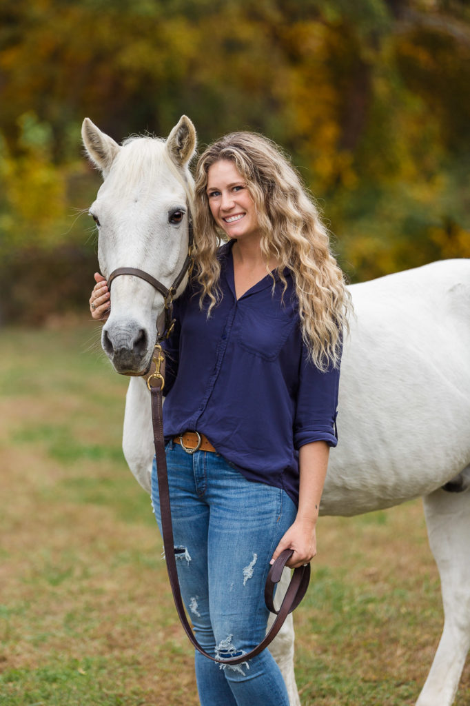 Carly posing with her white senior horse Hercules at Winward Equestrian