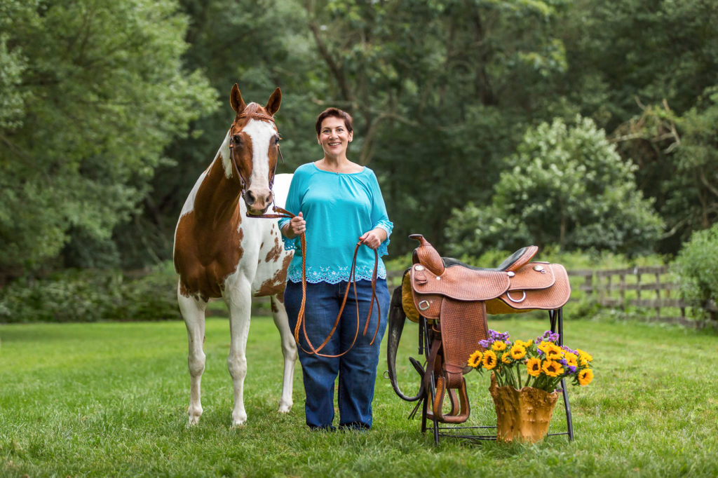 Joanne with her mare, Brandy, and their saddle with some sunflowers