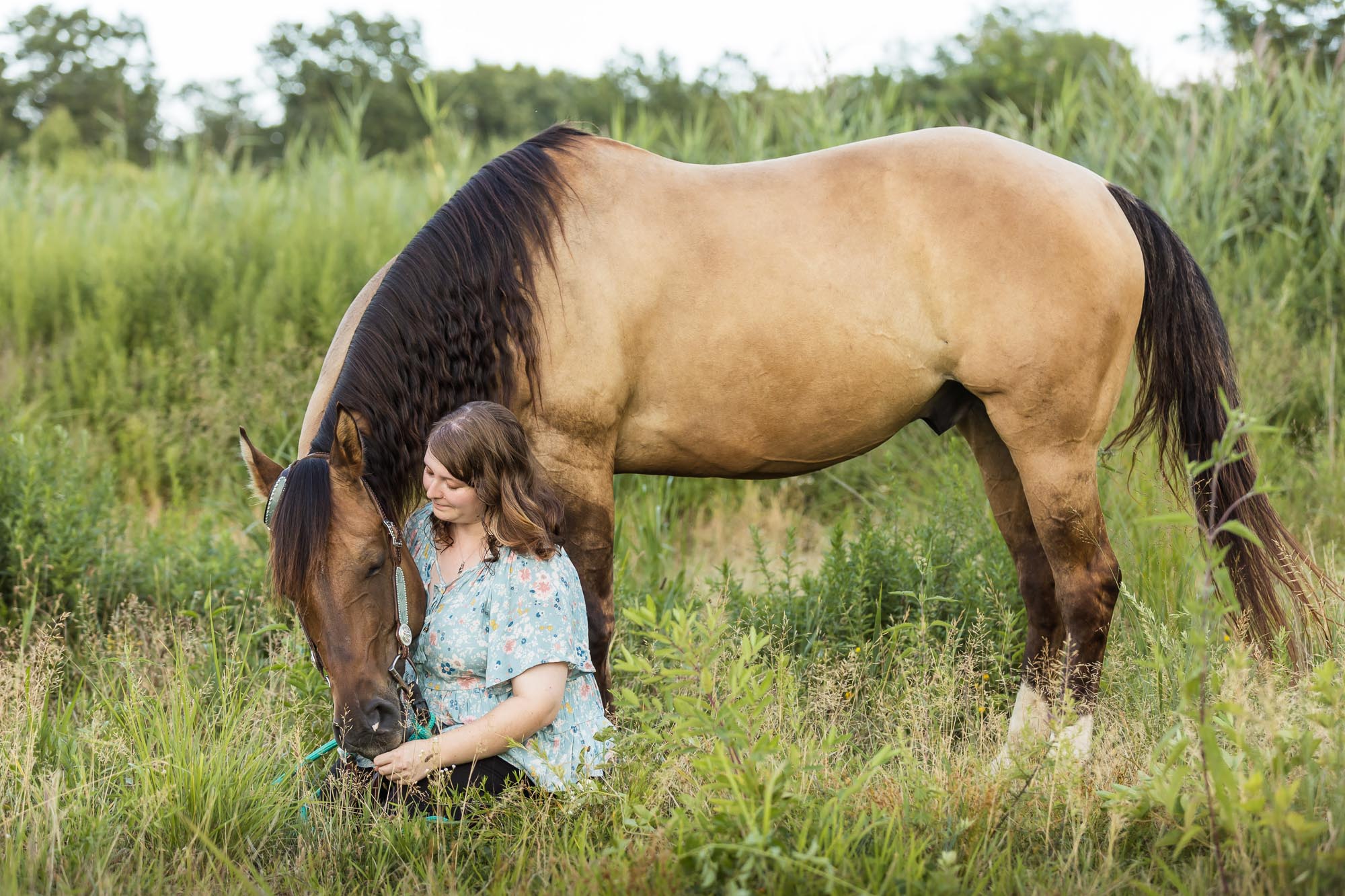 girl in blue shirt sitting in grass with her horse